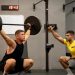 Man lifting weights under coach supervision in a gym setting, focusing on strength training.