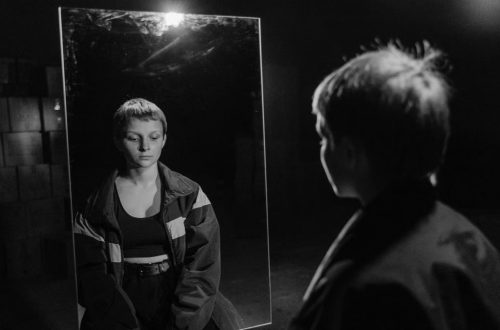 Black and white photo of woman with short hair reflecting in mirror, creating a contemplative mood.